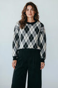 Plaza d'Amanté model wearing a black, grey, and white argyle knit crewneck sweater with ribbed trim and relaxed fit.