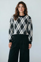 Plaza d'Amanté model wearing a black, grey, and white argyle knit crewneck sweater with ribbed trim and relaxed fit.