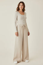 Model wearing a Plaza d'Amanté beige ribbed henley top and wide-leg drawstring lounge trousers in a studio setting.