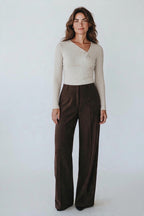 Plaza d'Amanté beige long sleeve twisted neckline top paired with dark brown wide leg trousers on a woman