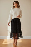 Plaza d'Amanté black floral lace midi skirt with a scalloped hem worn by a woman with a cream knit sweater