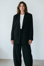 Plaza d'Amanté black oversized blazer with notched lapels and double-button closure worn by a woman over a white tee.