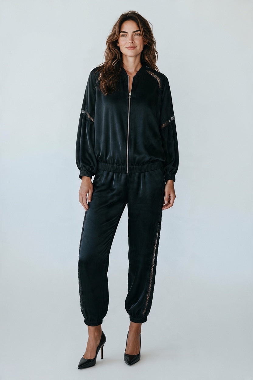 Model wearing a Plaza d'Amanté black satin lounge set with lace-trimmed bomber jacket and matching joggers.