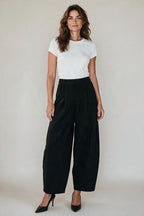 Plaza d'Amanté high-waisted black wide-leg tailored trousers worn by a woman with a white t-shirt and black heels.