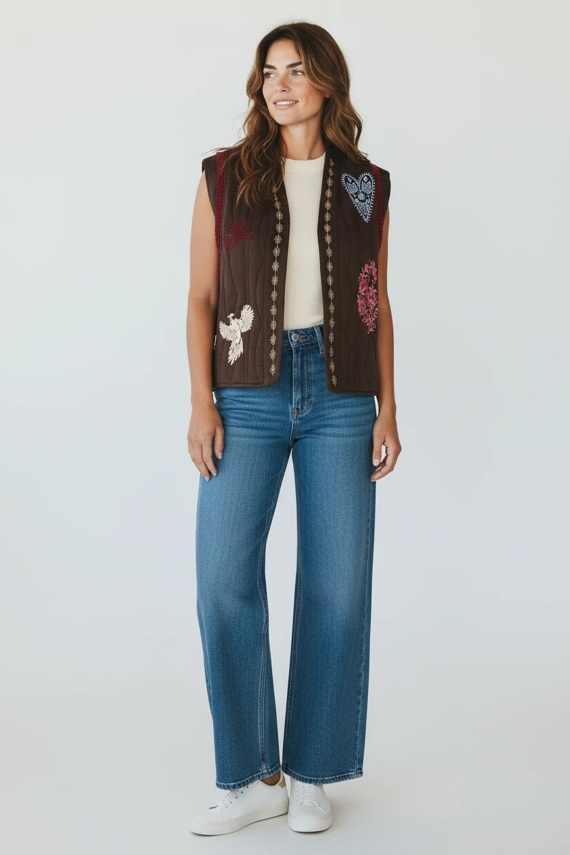 Model wearing a Plaza d'Amanté brown quilted sleeveless vest with colorful bird and heart embroidery over a white top.