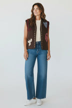 Model wearing a Plaza d'Amanté brown quilted sleeveless vest with colorful bird and heart embroidery over a white top.