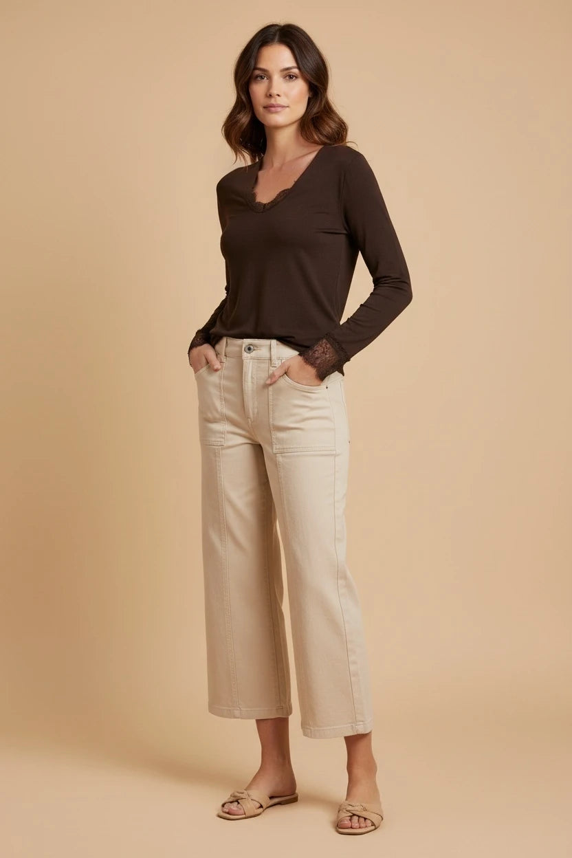 Plaza d'Amanté dark brown long sleeve top with V-neck and lace trim on neckline and cuffs worn with beige trousers.