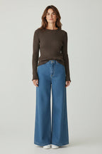 Plaza d'Amanté espresso brown ribbed long-sleeve knit sweater with lettuce-edge trim worn with wide-leg blue jeans.