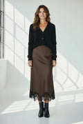 Plaza d'Amanté brown satin midi skirt with black lace hem worn by a woman with a black cardigan and ankle boots