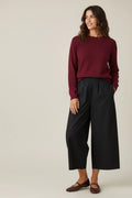 Plaza d'Amanté deep burgundy crewneck knit sweater worn by a woman with black wide-leg trousers and brown flats.