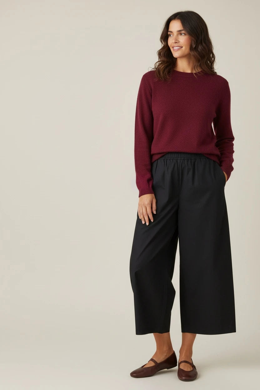 Plaza d'Amanté deep burgundy crewneck knit sweater worn by a woman with black wide-leg trousers and brown flats.