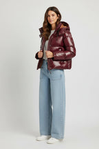 A model wearing a Plaza d'Amanté deep burgundy high-shine hooded puffer jacket with a cropped fit and front zipper.