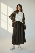 Plaza d'Amanté chocolate brown high-waisted maxi skirt with a drawstring waist and side pockets on a smiling model.