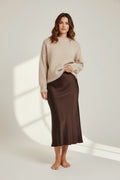 Plaza d'Amanté chocolate brown satin midi skirt worn by a model with a beige knit sweater on a neutral background.