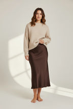 Plaza d'Amanté chocolate brown satin midi skirt worn by a model with a beige knit sweater on a neutral background.
