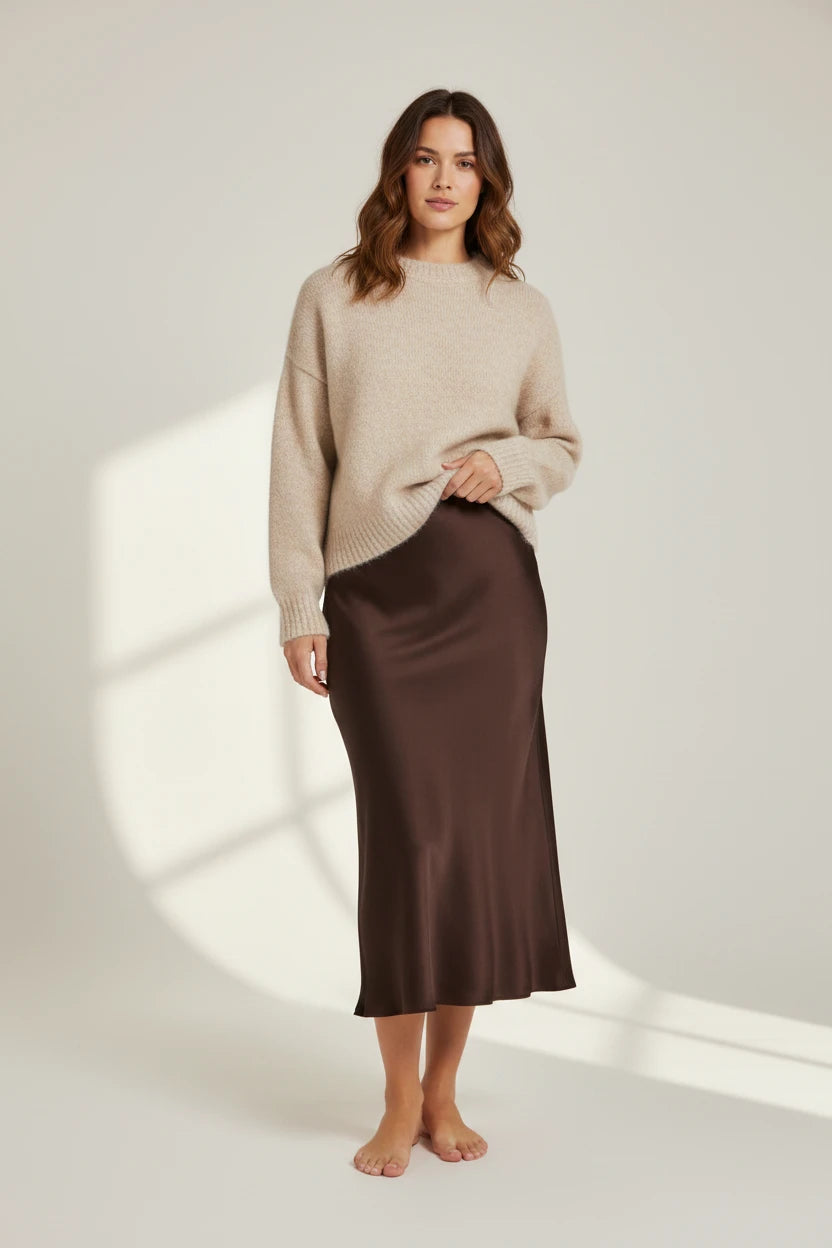 Plaza d'Amanté chocolate brown satin midi skirt worn by a model with a beige knit sweater on a neutral background.