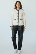 Plaza d'Amanté cream boucle jacket with black contrast piping, collarless design, and button front on a female model.