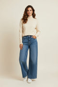 Plaza d'Amanté model wearing a cream turtleneck sweater and high-waisted wide-leg blue denim jeans with white sneakers