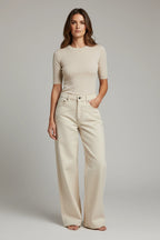 Plaza d'Amanté model wearing a beige fine-knit short-sleeve sweater and cream high-waisted wide-leg denim trousers.