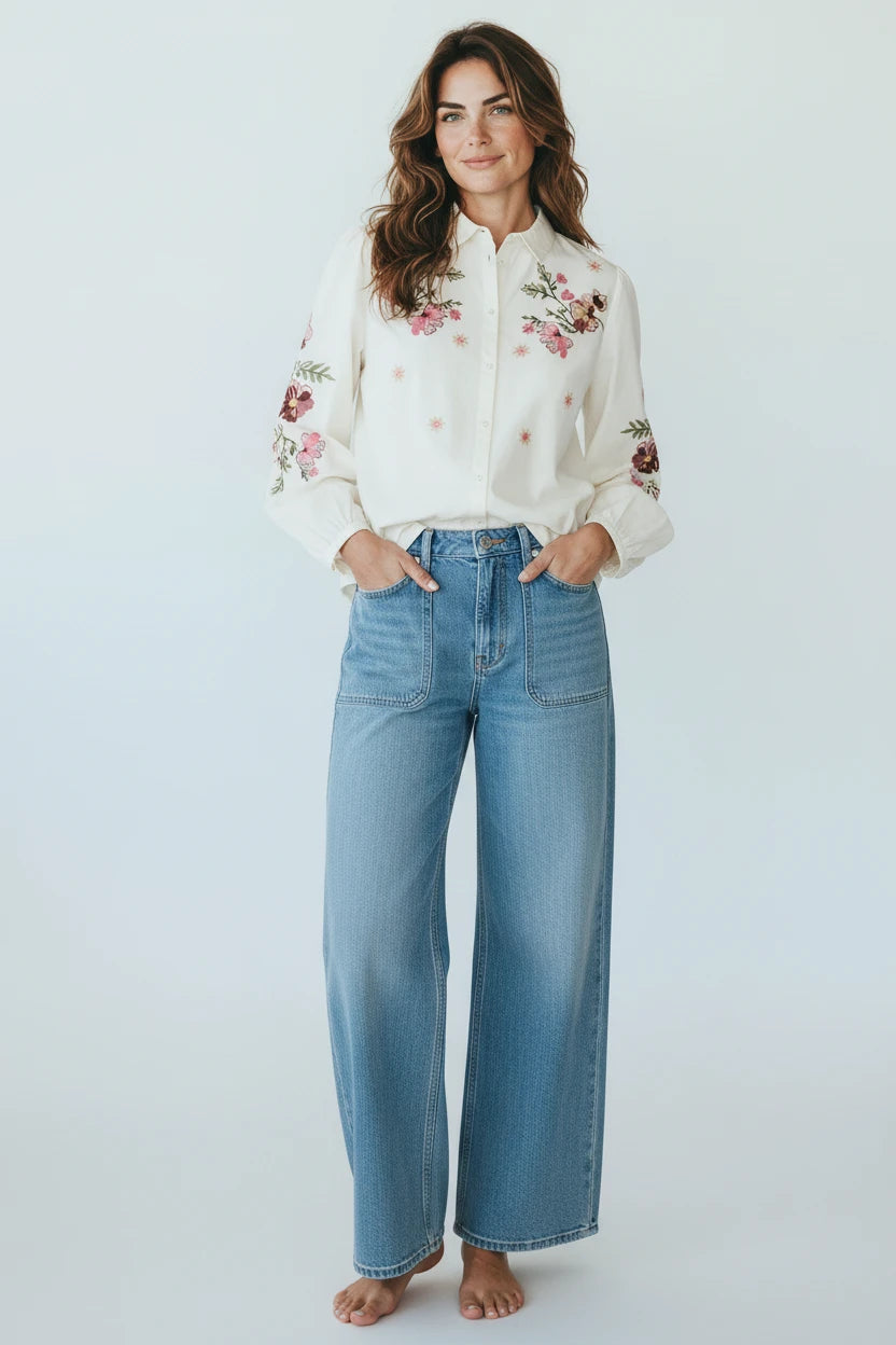 Plaza d'Amanté off-white button-down shirt with floral embroidery on chest and sleeves, worn with wide-leg blue jeans.