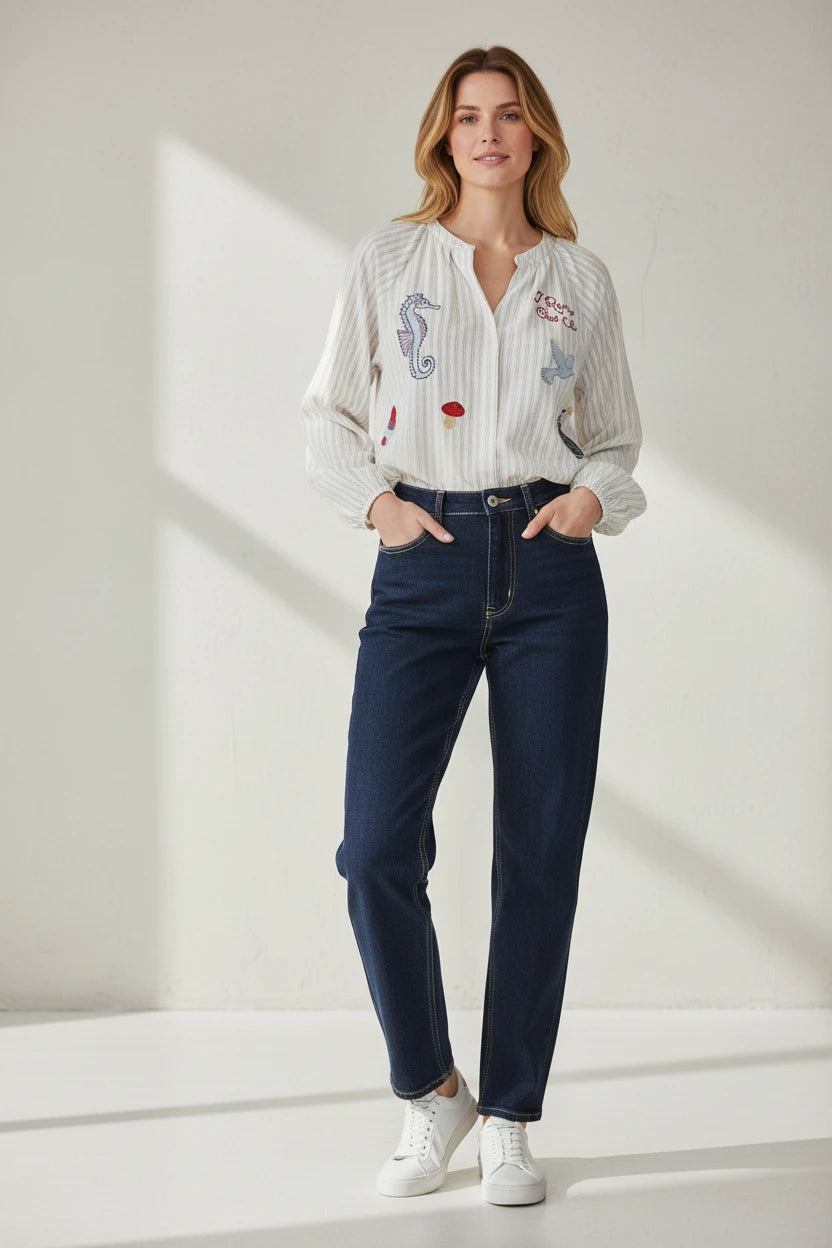 Plaza d'Amanté long sleeve pinstripe blouse with colorful seahorse and bird embroidery worn with dark denim jeans.