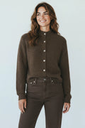 A smiling woman wearing a Plaza d'Amanté espresso brown mock neck knit cardigan with a button-down front.