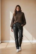Plaza d'Amanté model wearing a chunky chocolate brown turtleneck sweater and black high-waisted faux leather trousers.