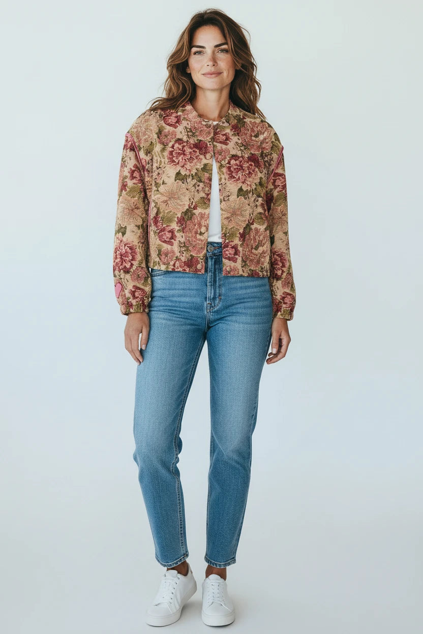 Model wearing a Plaza d'Amanté floral tapestry bomber jacket with earthy tones, paired with blue jeans and sneakers.