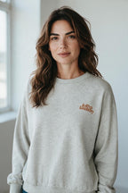 Plaza d'Amanté model wearing a heather grey Lollys Laundry crewneck sweatshirt with brown embroidered chest logo