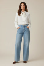 Plaza d'Amanté high-rise wide-leg light-wash denim jeans with front patch pockets worn by a woman in a white blouse.