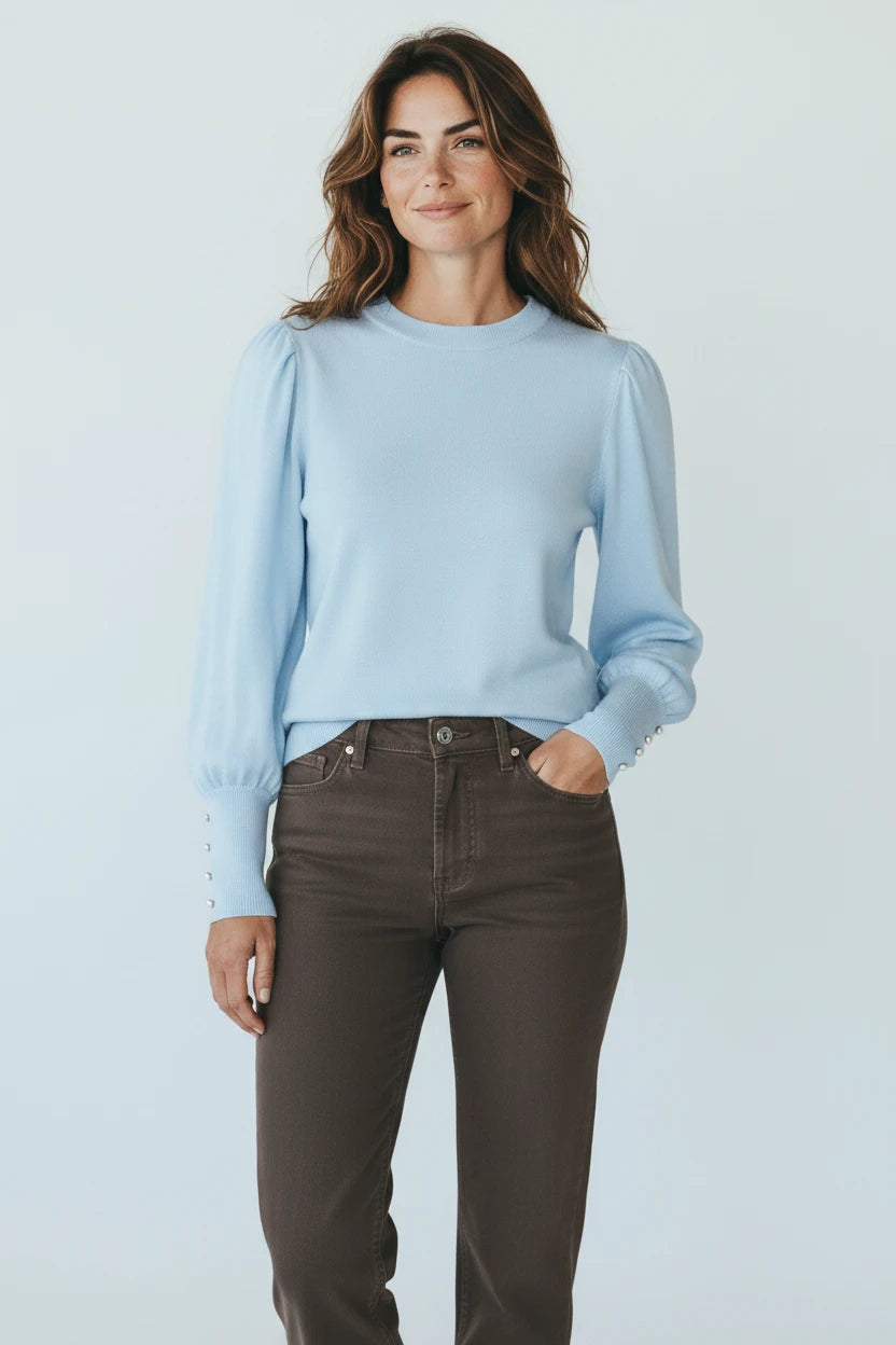 Plaza d'Amanté light blue crew neck sweater with puff sleeves and faux-pearl button cuffs worn by a smiling woman.