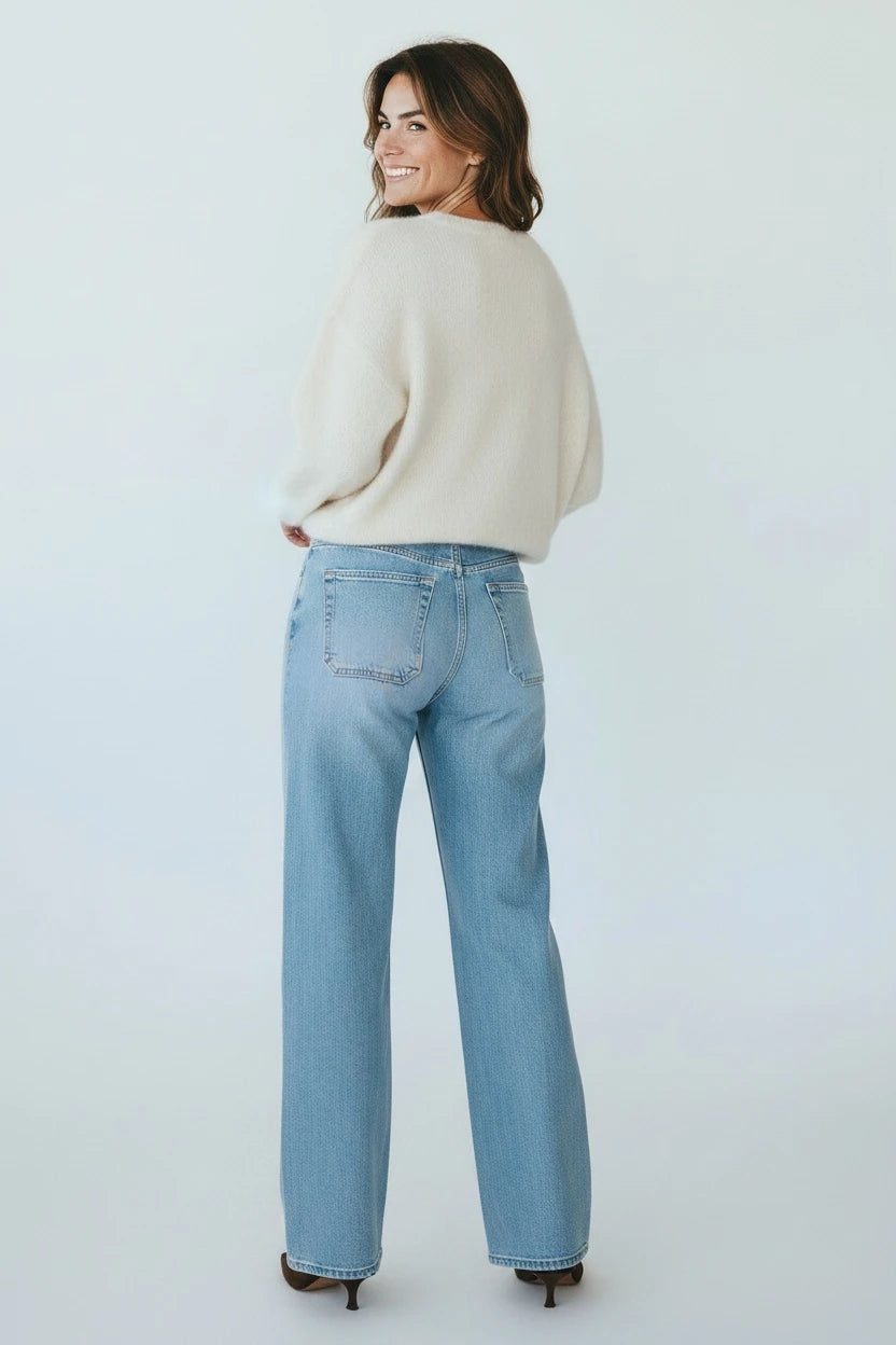 A woman wearing Plaza d'Amanté light-wash high-rise wide-leg denim jeans and a cream sweater, viewed from behind.