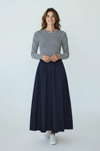 Plaza d'Amanté navy blue A-line maxi skirt worn by a smiling woman with a striped long-sleeve top and white sneakers.