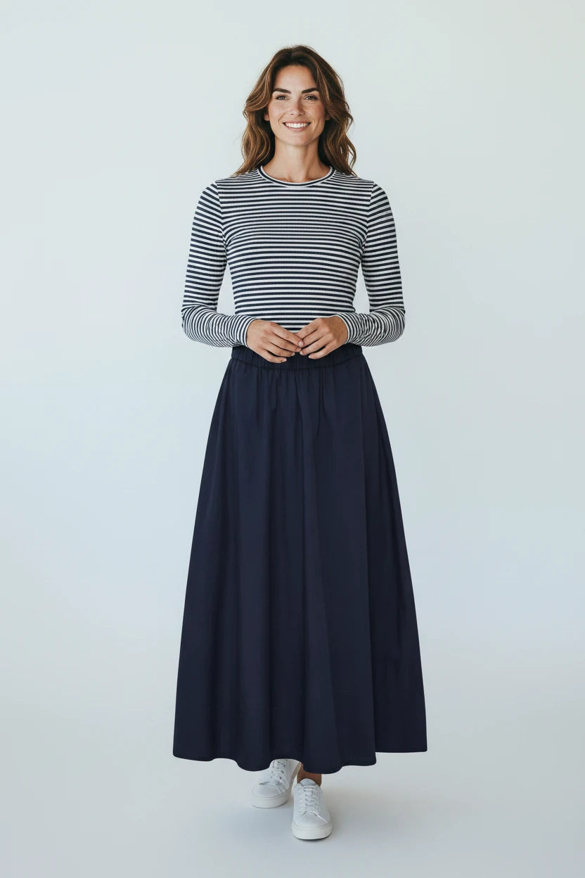 Plaza d'Amanté navy blue A-line maxi skirt worn by a smiling woman with a striped long-sleeve top and white sneakers.
