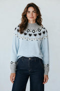 Model wearing a Plaza d'Amanté sky-blue knit sweater with a grey mock neck and Nordic heart and geometric patterns.