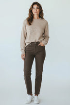 Plaza d'Amanté oatmeal crewneck sweater and chocolate brown straight-leg denim jeans worn by a woman with sneakers.