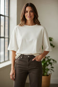 Plaza d'Amanté off-white relaxed fit cotton crewneck t-shirt worn by a woman with brown hair in a bright room.