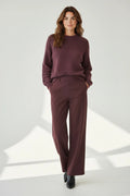 Plaza d'Amanté model wearing a deep plum textured knit sweater and matching high-waisted wide-leg tailored trousers.