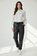 Plaza d'Amanté model wearing a white polka dot tie neck blouse and black faux leather joggers with white sneakers.