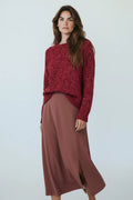 Plaza d'Amanté model wearing a deep red marled knit crewneck sweater and a clay-toned midi skirt with a side slit.