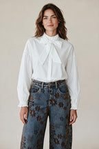 Plaza d'Amanté white long sleeve blouse with a neck tie bow and ruffled cuffs worn with floral print denim jeans