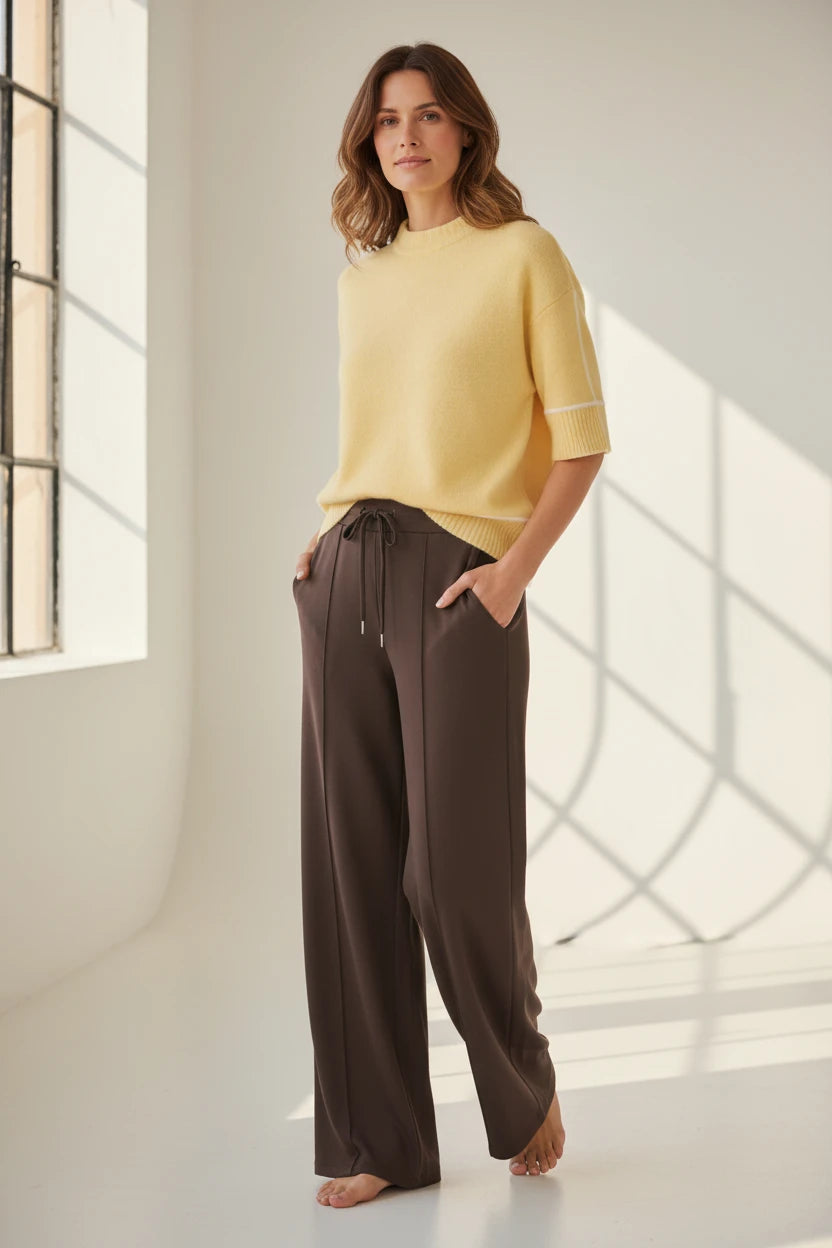 Plaza d'Amanté model wearing a buttery yellow mock neck knit sweater and chocolate brown wide-leg drawstring trousers.